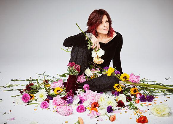 Rosanne Cash sitting and surrounded by cut flowers.